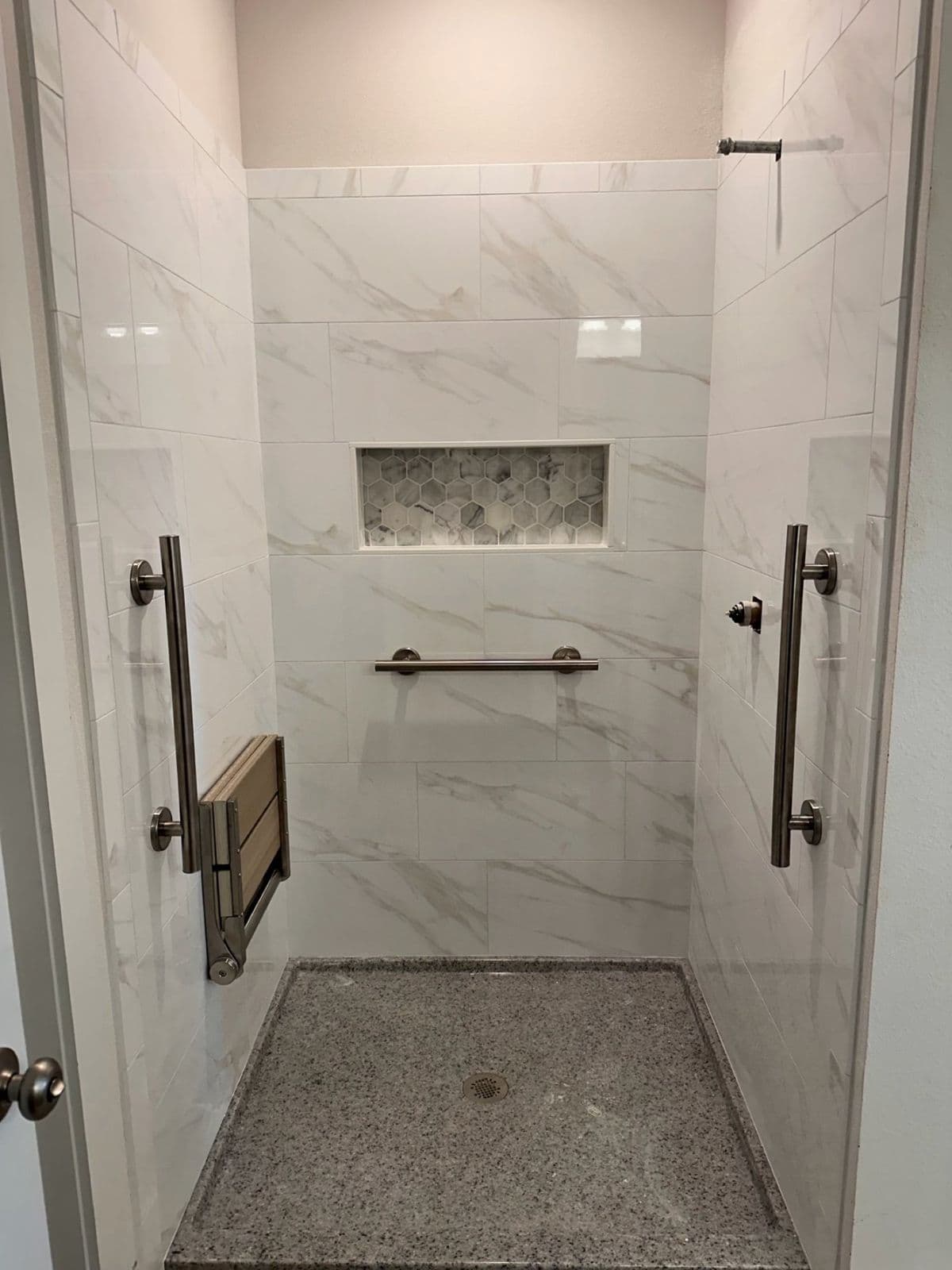 Accessible shower installation in Pensacola, FL: marble look tile with grab bars, fold down seat, and mosaic floor in Pensacola, FL