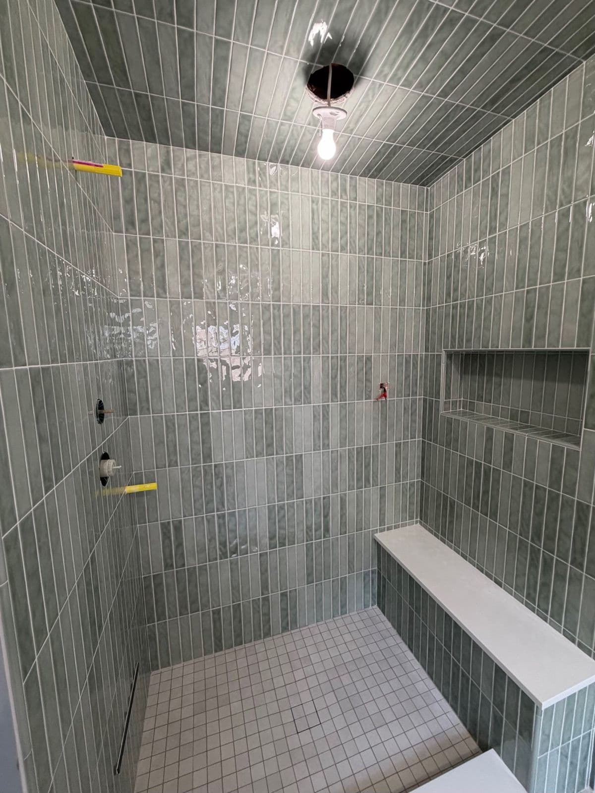 Custom shower installation in progress in Pensacola, FL: green vertical tile with bench and niche over the waterproofing, before fixtures