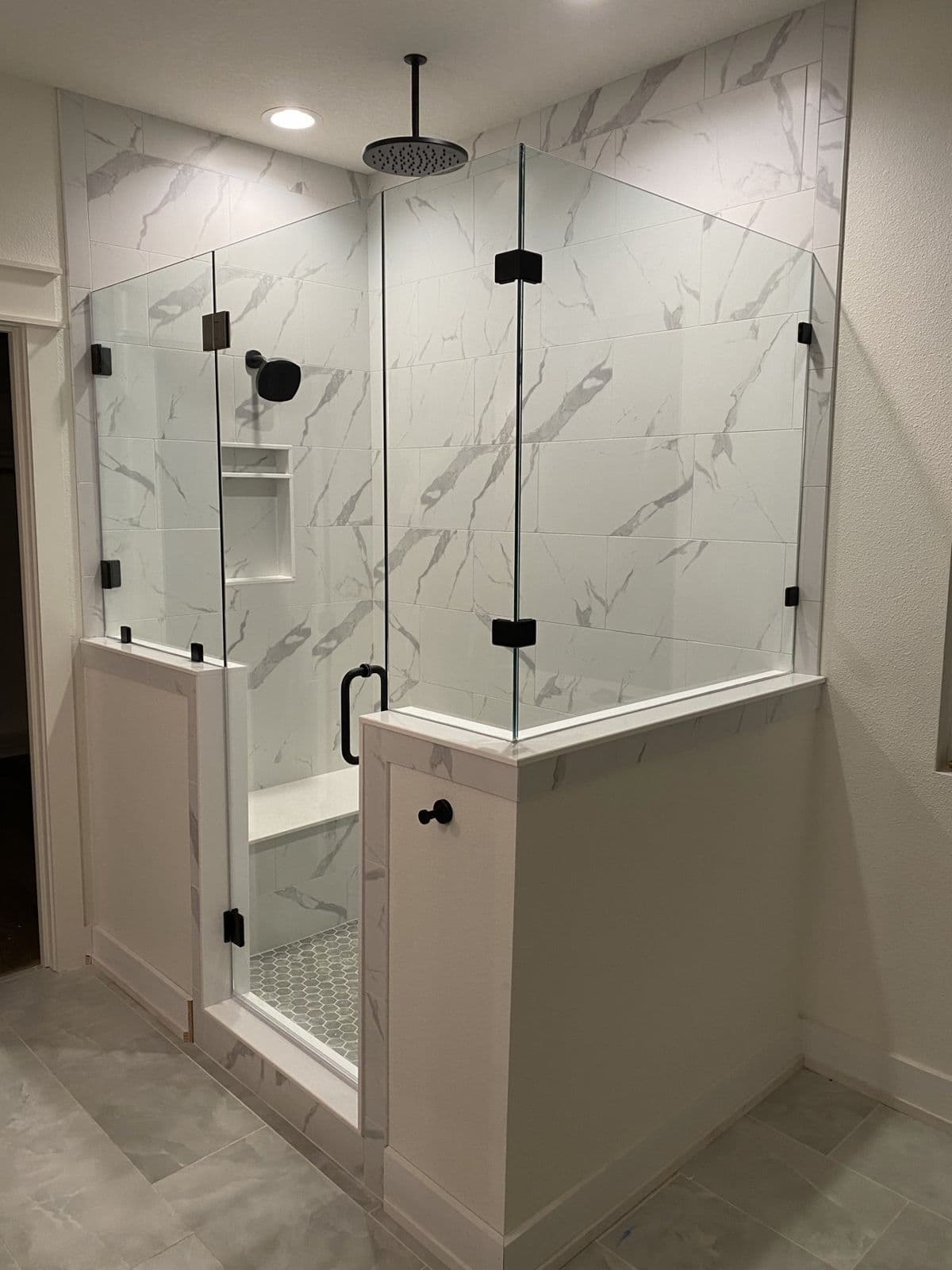 Custom tile shower installation in Pensacola, FL: marble look shower with black hardware frameless glass and tiled half walls