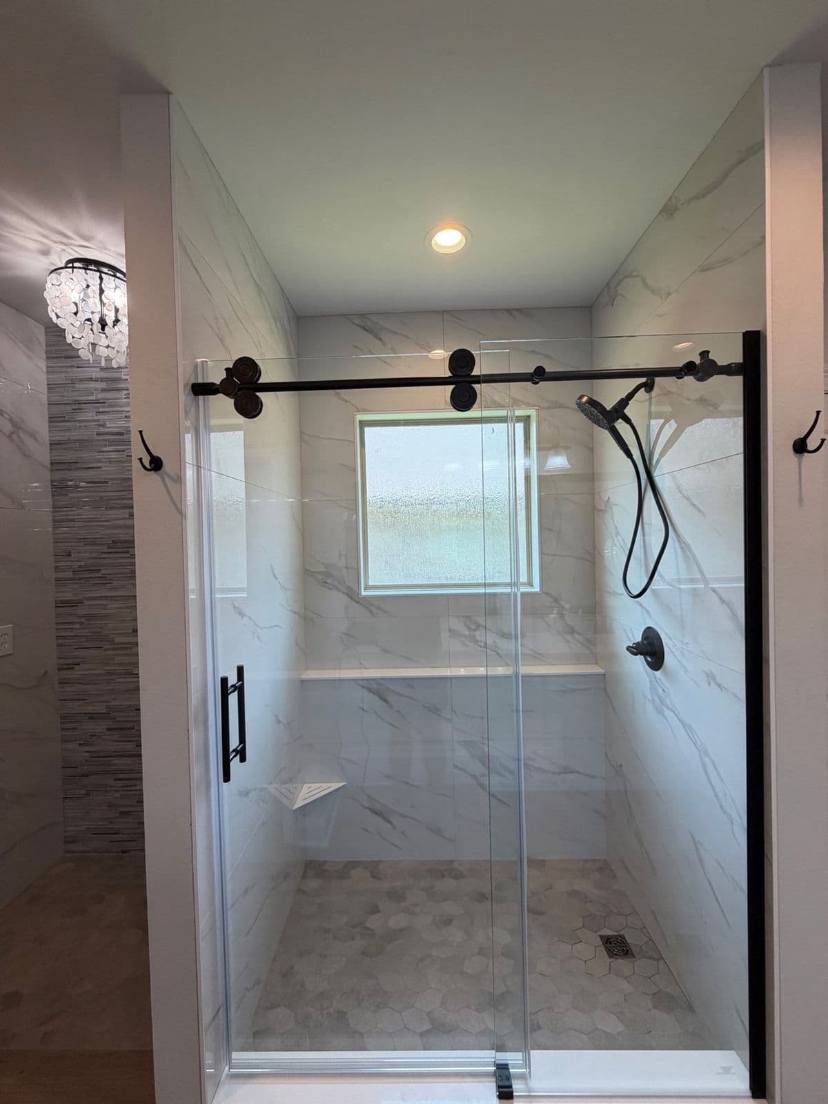 Custom shower installation in Pensacola, FL: marble look porcelain shower with black sliding glass door, bench, and window by Custom Tile & Design