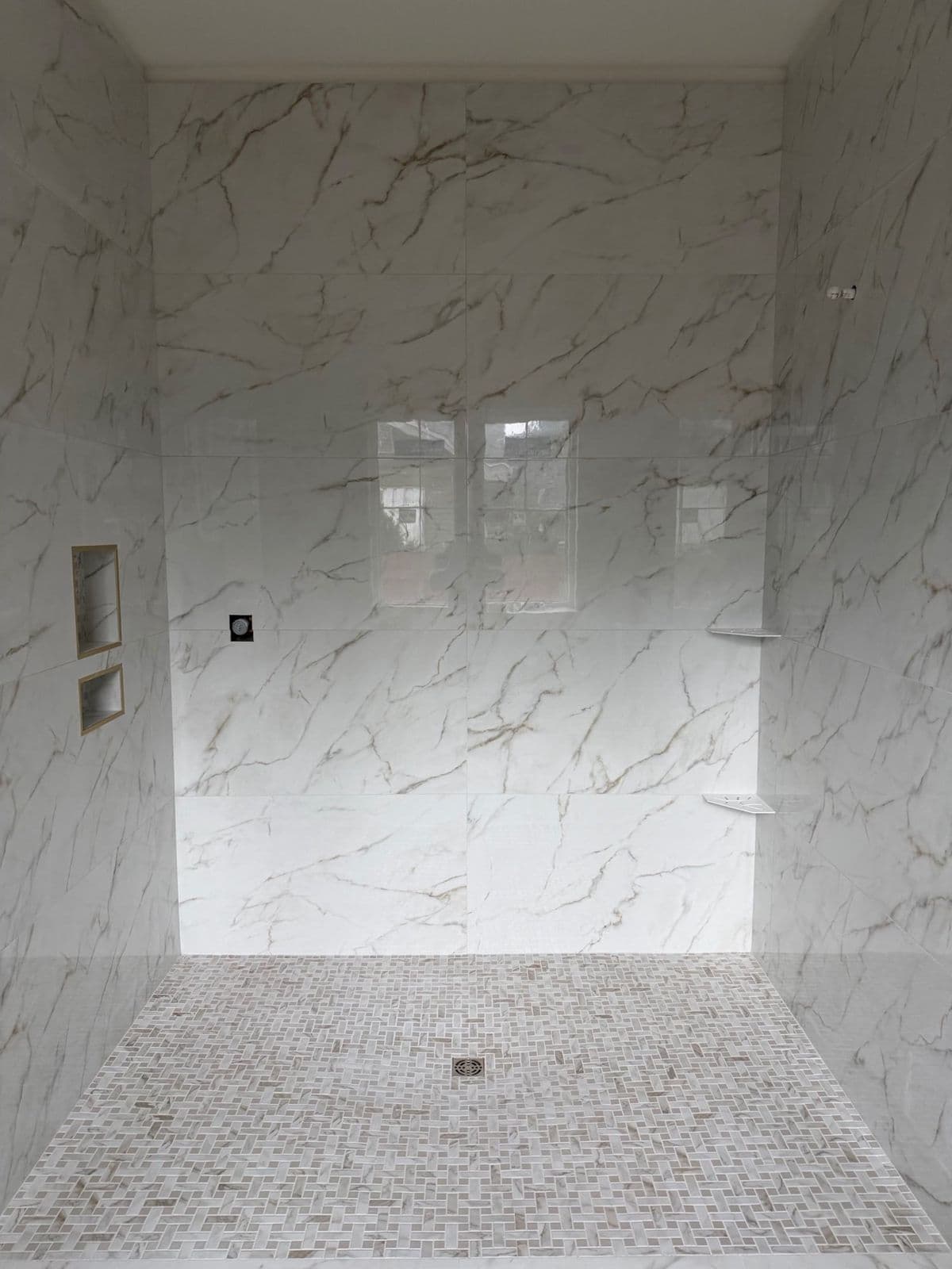 Custom tile shower in Pensacola, FL: marble look porcelain walls and mosaic floor over a bonded waterproofing membrane, before fixtures