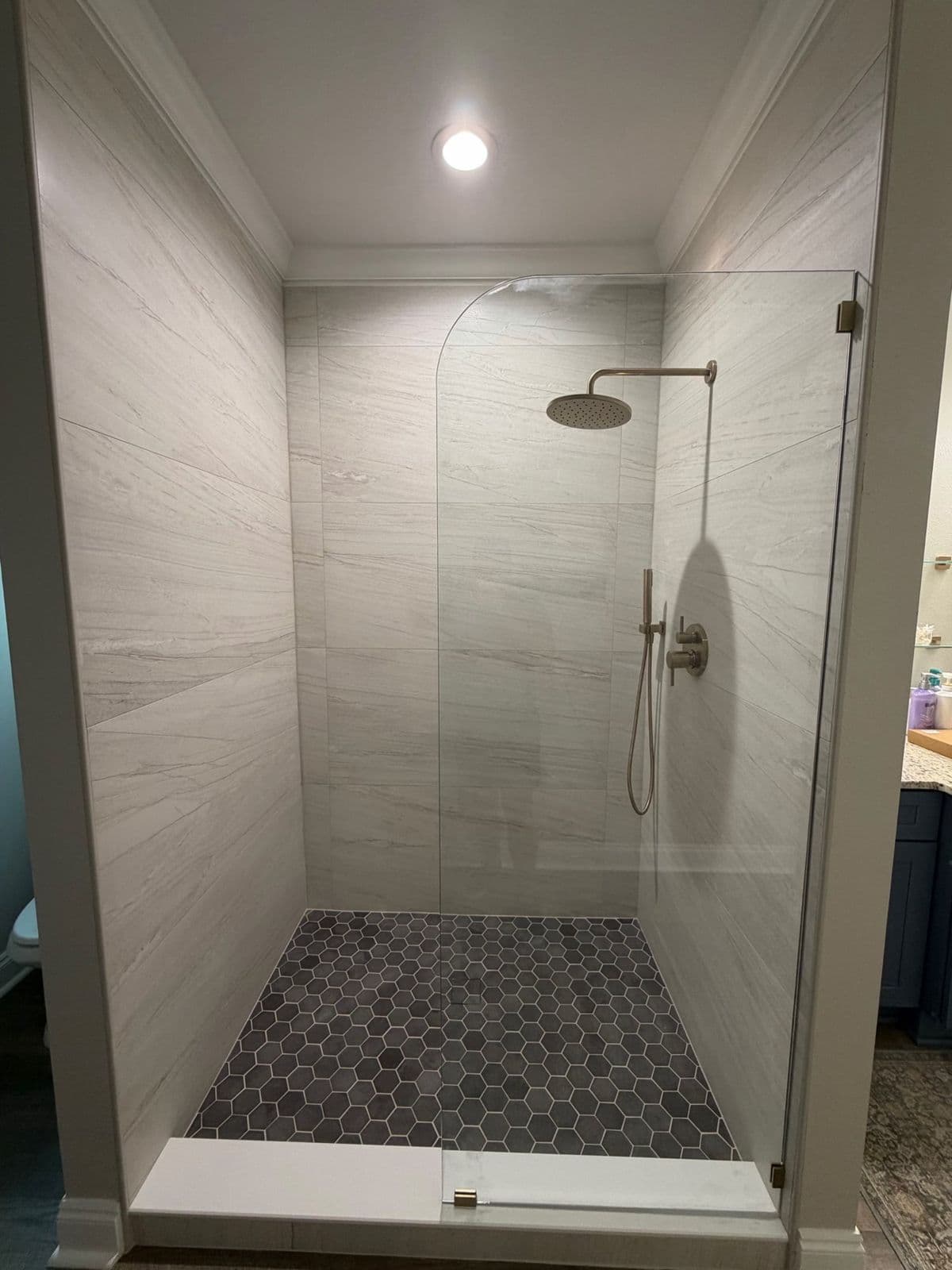 Curbless shower installation in Pensacola, FL: white large format tile with grey hexagon mosaic floor