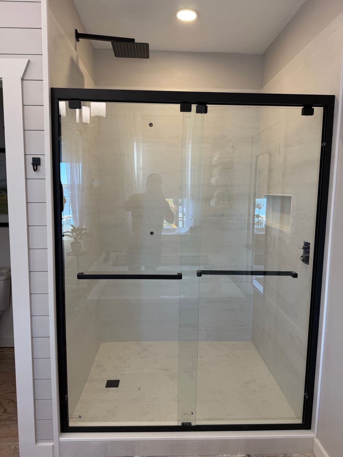 Tile shower installation in Pensacola, FL: white large format shower with black framed sliding glass door
