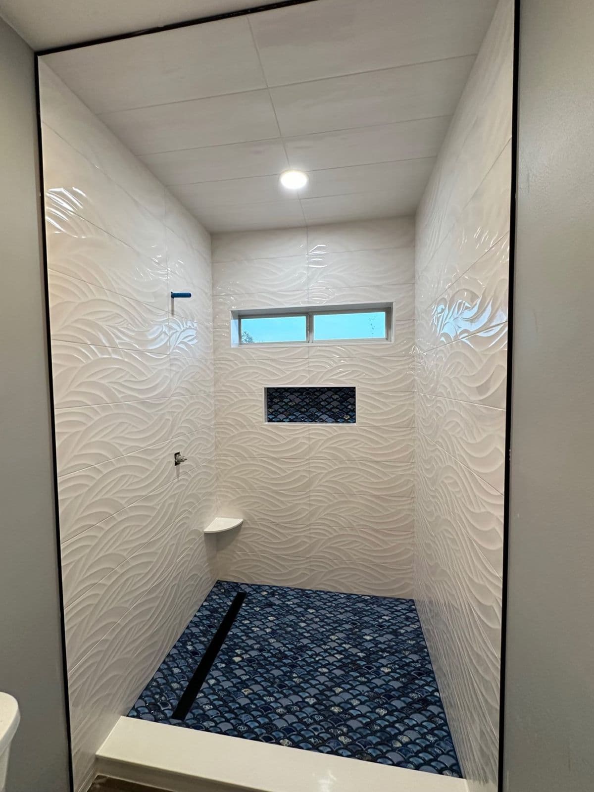 Custom tile shower installation in Pensacola, FL: white wave textured tile shower with blue mosaic floor by Custom Tile & Design